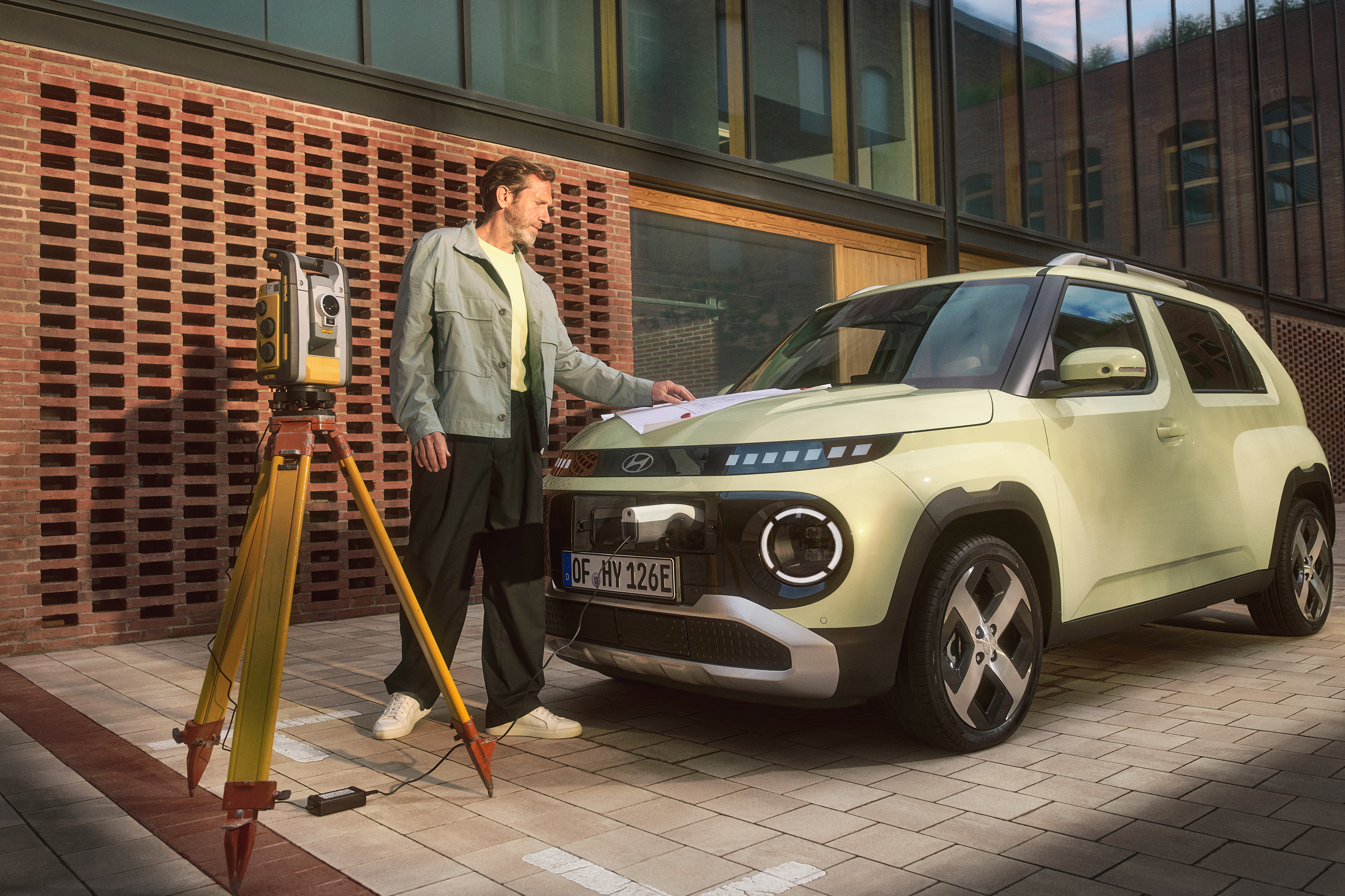 Person consulting plans beside the INSTER with a tripod instrument nearby and a cable connected to the vehicle.